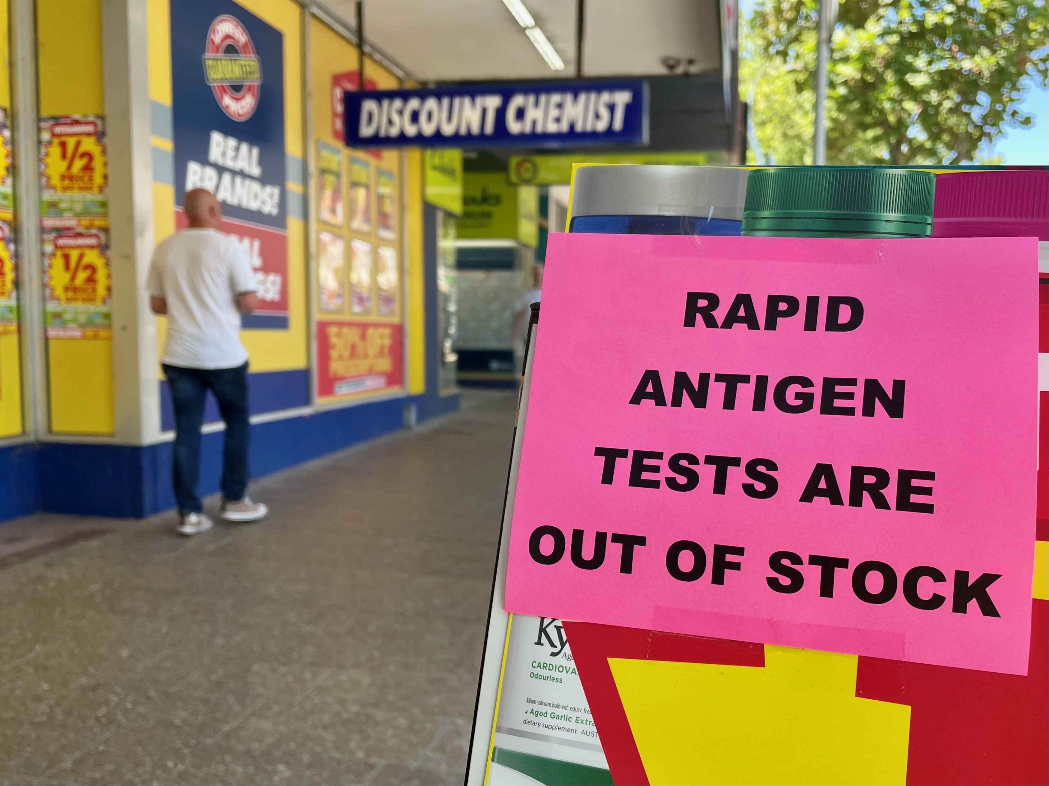 A pink sheet of paper with black text reads 'RAPID ANTIGEN TESTS ARE OUT OF STOCK'.